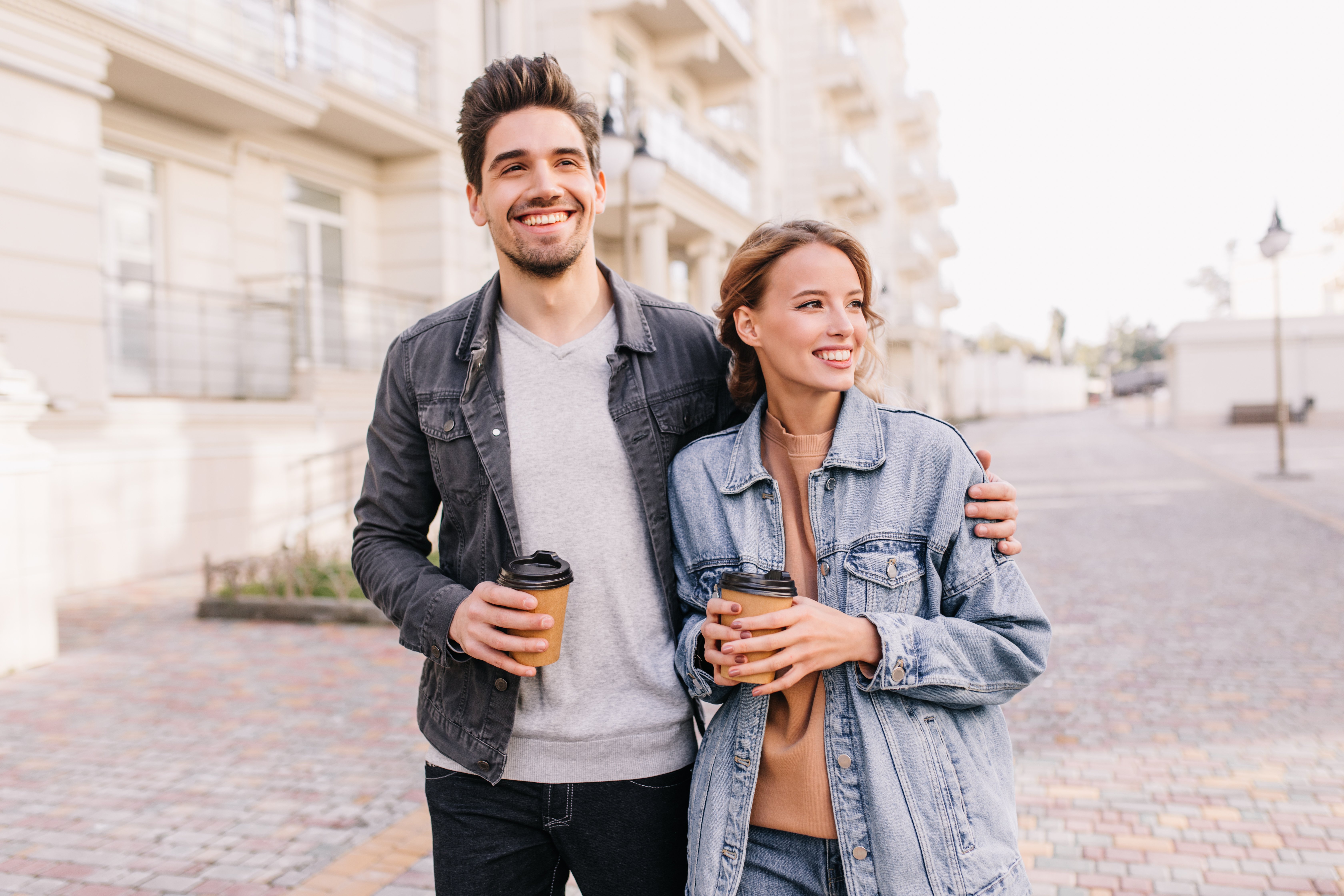 handsome-young-man-holding-cup-coffee-embracing-girlfriend-smiling-couple-enjoying-outdoor-date